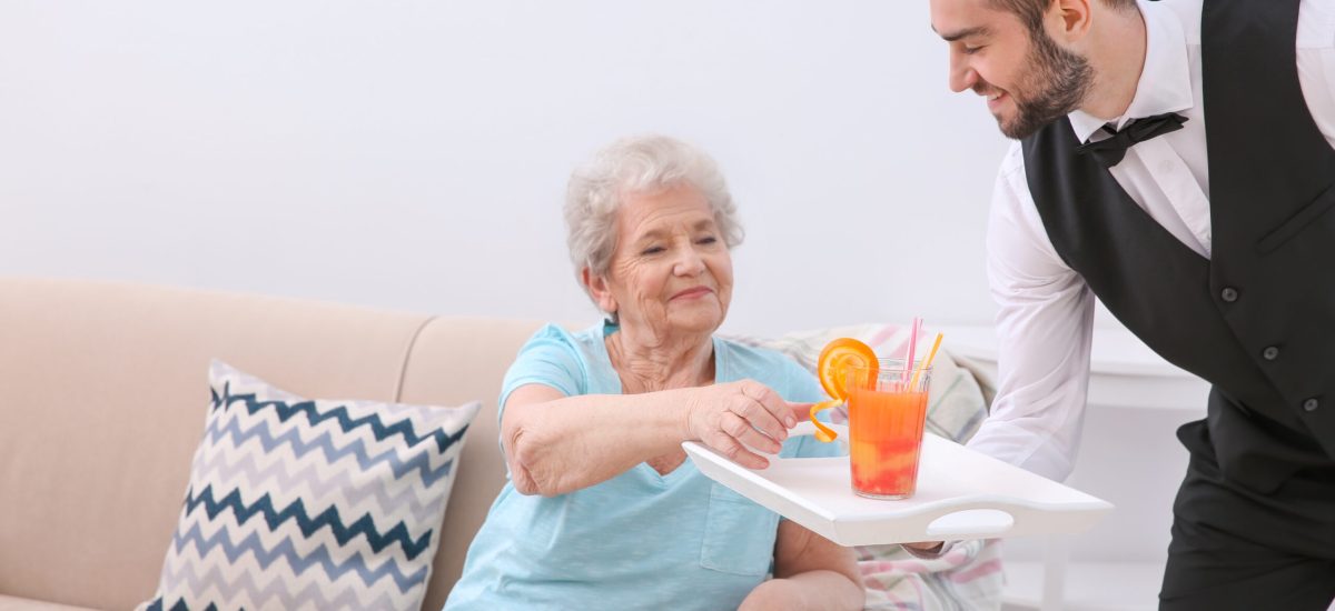 Young man serving glass of juice for elderly woman. Concept of nursing
